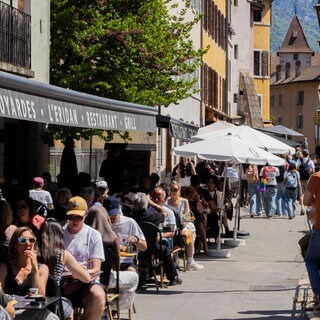 Menschen sitzen auf der Terrasse eines Restaurants am Fluss Thiou in der Altstadt. Annecy, Frankreich. Symbolfoto.