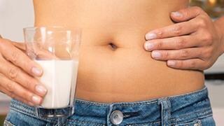 Frau mit einem Glas Milch hält sich die Hand auf den schmerzenden Bauch.