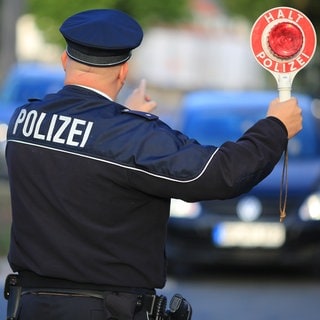 Bei einer Verkehrskontrolle hält ein Polizist eine Kelle in die Höhe.