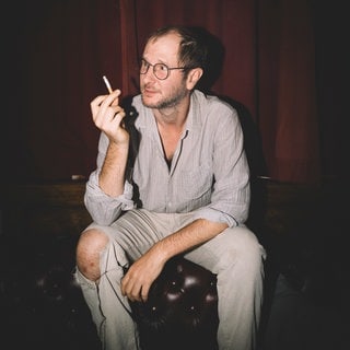 Musiker Marco Wanda hält eine Zigarette in der Hand und schaut von der Kamera weg. 
