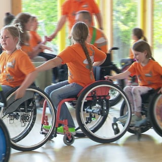 Kinder sitzen in einem Rollstuhl und fahren hintereinander.