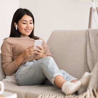 Frau sitzt auf einem Sofa und hört mit Kopfhörern Musik