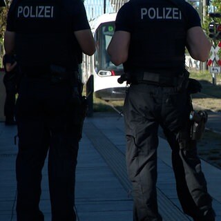 Zwei Polizisten warten an einer Straßenbahnhaltestelle.