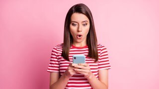 Eine Frau schaut überrascht auf ihr Smartphone.