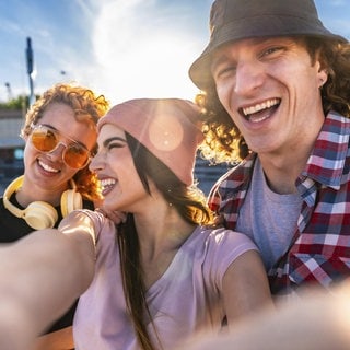 Drei Freunde machen fröhlich ein Selfie im Freien: Mit anderen Menschen auf gleicher Wellenlänge zu sein, fühlt sich gut an. Man kommt schnell ins Gespräch, weiß wie der andere tickt und muss nicht viel erklären: Es vibet eben einfach. 