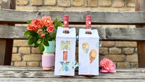 Gebasteltes Geldgeschenk für Hochzeit, Geburtstag oder Taufe an Flaschen auf einer Bank mit Blumen