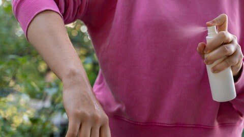 Eine Frau sprüht ihren Arm mit einem Mücken-abwehrenden Spray für die Haut ein.