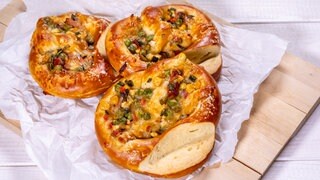Drei fertig gebackene mit Gemüse und Schinken gefüllte Brezeln liegen im Dreieck ein wenig übereinander auf einem Holzbrett