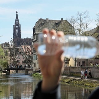 Symbolbild: Ein Mann trinkt einen Schluck Wasser aus einer Flasche. Im Hintergrund ist die Kathedrale von Straßburg zu sehen.