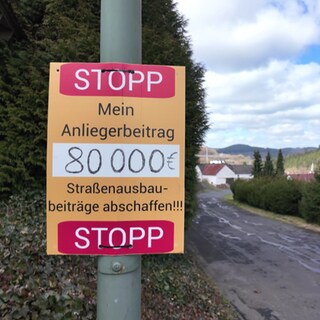 Auf einem Schild steht: "STOPP - Mein Anliegerbetrag 80.000€ - Straßenausbau-beiträge abschaffen!"