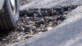 Ein Auto fährt durch ein Schlagloch | Schaden durch Schlaglöcher: Das könnt ihr tun