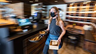Eine Kellnerin mit Mundschutz trägt in einem Restaurant Essensteller. 