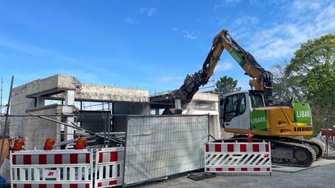 Abriss Turmbergbahn in Karlsruhe-Durlach: Ein gelber Bagger reißt ein Stück aus dem Gerippe eines grauen Betongebäudes.