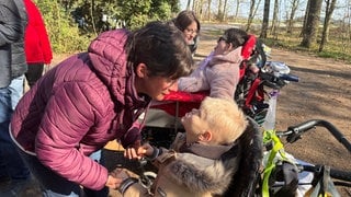 Zwei Menschen sitzen im Rollstuhl im Wald. Mimi und Jannis sind seit Geburt schwerstbehindert. Gemeinsam mit Betreuern von der Lebenshilfe Mayen testen sie bei sonnigem Frühlingswetter den Rollstuhlwanderweg in Mayen.