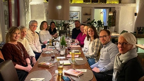 Mehrere Menschen sitzen an einem Tisch - vor ihnen liegen Bücher.