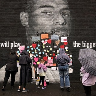 Menschen platzieren Unterstützungsbotschaften über dem beleidigenden Schriftzug auf dem Wandbild von Manchester-United-Stürmer und England-Spieler Marcus Rashford. Das Wandbild wurde am Morgen nach der Niederlage der englischen Fußballmannschaft zerstört. Mit Empörung haben Politik, Fußballverband und Gesellschaft in Großbritannien auf rassistische Beleidigungen gegen die englischen Elfmeter-Fehlschützen im EM-Finale im Juli 2021 reagiert.