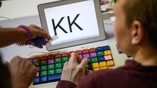 Eine bunte Tastatur und ein "K" auf Zettel und Bildschirm: Eine Therapeutin übt mit einem autistischen Kind das Erkennen und Schreiben von Buchstaben. Im Alb-Donau-Kreis soll die Betreuung für Menschen mit Autismus verbessert werden. Einige Maßnahmen laufen bereits. 