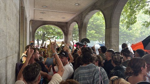 Menschen feiern in Stuttgart beim CSD Stuttgart 2025 in einer Passage, weil es wieder zu regnen begonnen hat.