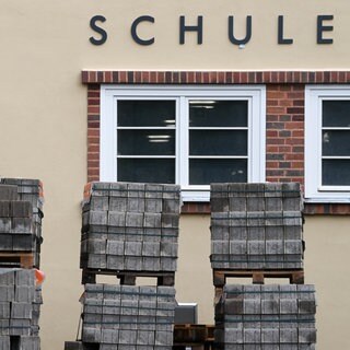 (Symbolbild): Paletten mit Steinen liegen vor einer Schule, welches saniert wird. Erste Mittel aus dem Sondervermögen des Bundes kommt bei Kommunen an
