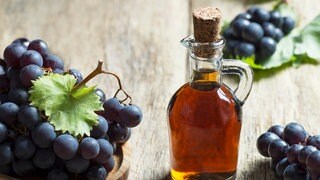 Flasche mit Essig, daneben steht ein Korb mit Trauben
