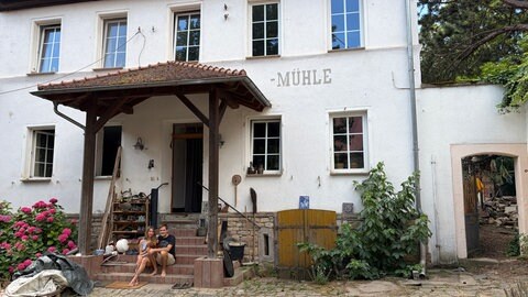 Mira und Tobias sitzen vor der alten Königsmühle in Gau-Odernheim. Gemeinsam mit anderen leben sie in diesem alternativen Wohnprojekt