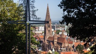 Ein stilisiertes Kreuz steht auf dem Freiburger Schlossberg während im Hintergrund das Münster zu sehen ist. Nach drei umstrittenen Personalentscheidungen wird das Erzbistum Freiburg stark kritisiert.