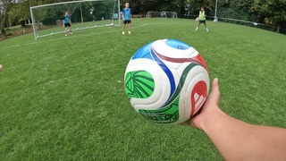 Eine Hand hält vor dem Tor einen Fußball. Im Hintergrund sind zwei Jugendliche. Durch den Wegfall verschiedener Regeln, sollen sie den Sinn von ihnen lernen.