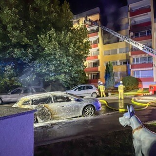 Vor einem Mehrfamilienhaus steht ein Feuerwehrauto mit Drehleiter, im Vordergrund steht ein Auto, das gebrannt hat. Bei einem Brand in Maichingen standen mehrere Wohnungen und zwei Autos in Flammen. 