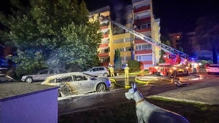 Vor einem Mehrfamilienhaus steht ein Feuerwehrauto mit Drehleiter, im Vordergrund steht ein Auto, das gebrannt hat. Bei einem Brand in Maichingen standen mehrere Wohnungen und zwei Autos in Flammen. 