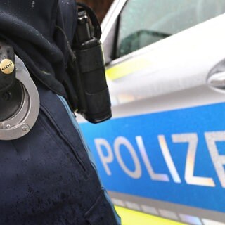 Ein Polizist mit Handschellen vor einem Polizeiauto. Eine Frau konnte vor ihrem Exfreund fliehen, nachdem dieser sie in Künzelsau entführt hatte.