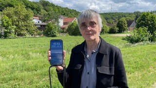 Die Ortsbürgermeisterin von Tiefenthal im Kreis Bad Kreuznach zeigt, dass sie auf der Landstraße keinen Empfang auf ihrem Handy hat.