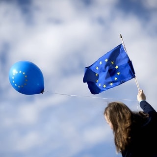 Eine Frau hält eine Europa-Fahne und einen Ballon in die Luft.