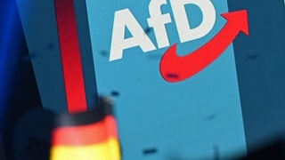 Ein Logo der AfD steht auf einer Wand auf einer Bühne beim AfD-Wahlkampfabschluss im Kultur- und Kongresshaus in Magdeburg. Im Vordergrund ist eine Deutschlandfahne zu sehen.