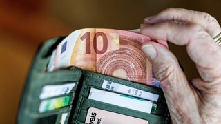 Ene Hand nimmt Geldscheine aus einem Portemonnaie.