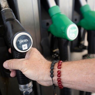 Ein Mann nimmt einen Zapfhahn an einer Tankstelle in die Hand.