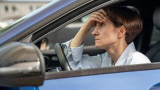 Ärger und Stress im Auto wegen Stau: Eine Autofahrerin stützt ihren Kopf auf die Hand und ist genervt vom Verkehr.