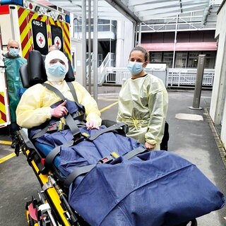 Ein Patient mit schweren Verbrennungen trägt Mundschutz und liegt auf einer Trage vor einem Krankenwagen. 