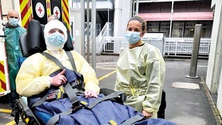 Ein Patient mit schweren Verbrennungen trägt Mundschutz und liegt auf einer Trage vor einem Krankenwagen. 