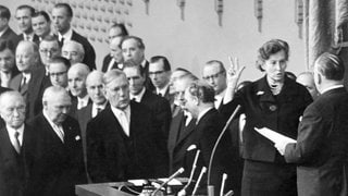 Als erste Frau wurde Elisabeth Schwarzhaupt (CDU) am 14. November 1961 durch den Bundestagspräsidenten Eugen Gerstenmaier (rechts) als Bundesministerin vereidigt. Sie wird das neu geschaffene Ministerium für Volksgesundheit leiten, das unter anderem Fragen der Reinhaltung des Wassers, der Luft und der Lärmbekämpfung zu bearbeiten hat. Vorn links Bundeskanzler Konrad Adenauer und Vizekanzler Ludwig Erhard.