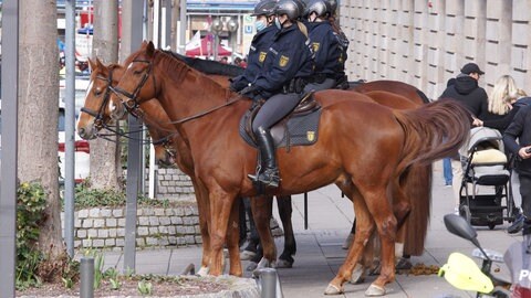 Berittene Polizistinnen stehen an einer Straße, während Teilnehmer einer Demonstration durch die Stadt ziehen.