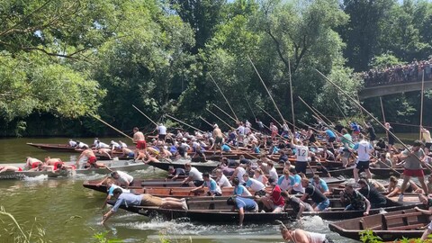 Beim Start des Tübinger Stocherkahnrennens 2025 legen sich die studentischen Teilnehmer mächtig ins Zeug: eine Person stochert mit einer Stange, die anderen paddeln mit den Armen.