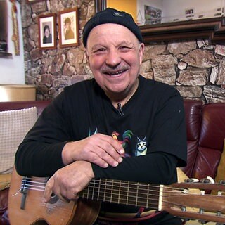 Der 76-jährige Yusuf Cavak hält seine Gitarre und lächtelt in die Kamera.