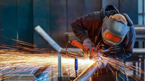 Ein Industriearbeiter flext mit einem Winkelschleifer ein Stahlrohr. Die IHK hat 200 Industriebetriebe und Dienstleister zum Standort Rheinland-Pfalz befragt.