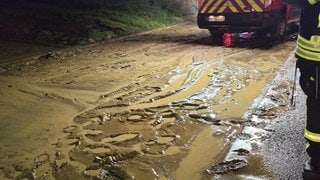 Braun gefärbtes Regenwasser und Schlamm stehen nach Starkregen auf der Straße bei Hardthausen am Kocher.