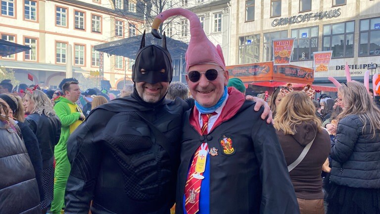 Zwei Männer in Kostümen stehen in der Koblenzer Alstadt. An Schwerdonnerstag in Koblenz ist auch Batman unterwegs. Mit dabei hat er seinen treuen Freund Flamingo.