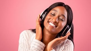 Junge Frau mit Kopfhörer lächelt glücklich mit geschlossenen Augen: Unser Musikgeschmack ist Teil unserer Identität. Wissenschaftler erforschen, wie und wann er sich bildet.