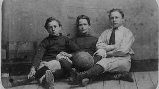 Drei Jungs in Sportkleidung mit Fußball, England um 1885: Wurde das Fußballspiel in England erfunden?
