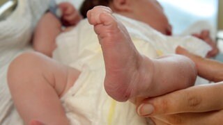 Eine Hand hält das Füßchen eines neugeborenen Babys. Eine Frau hat bei Wiesbaden ihr Kind im Auto zur Welt gebracht.