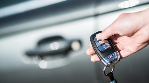 Eine Frau hält einen Autoschlüssel mit Druckknopf in der Hand.