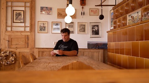 Ein Mann sitzt an einem Tisch. Gastwirt Martin Dold schaut alte Fotos vom Plattensee bei Sankt Peter an.